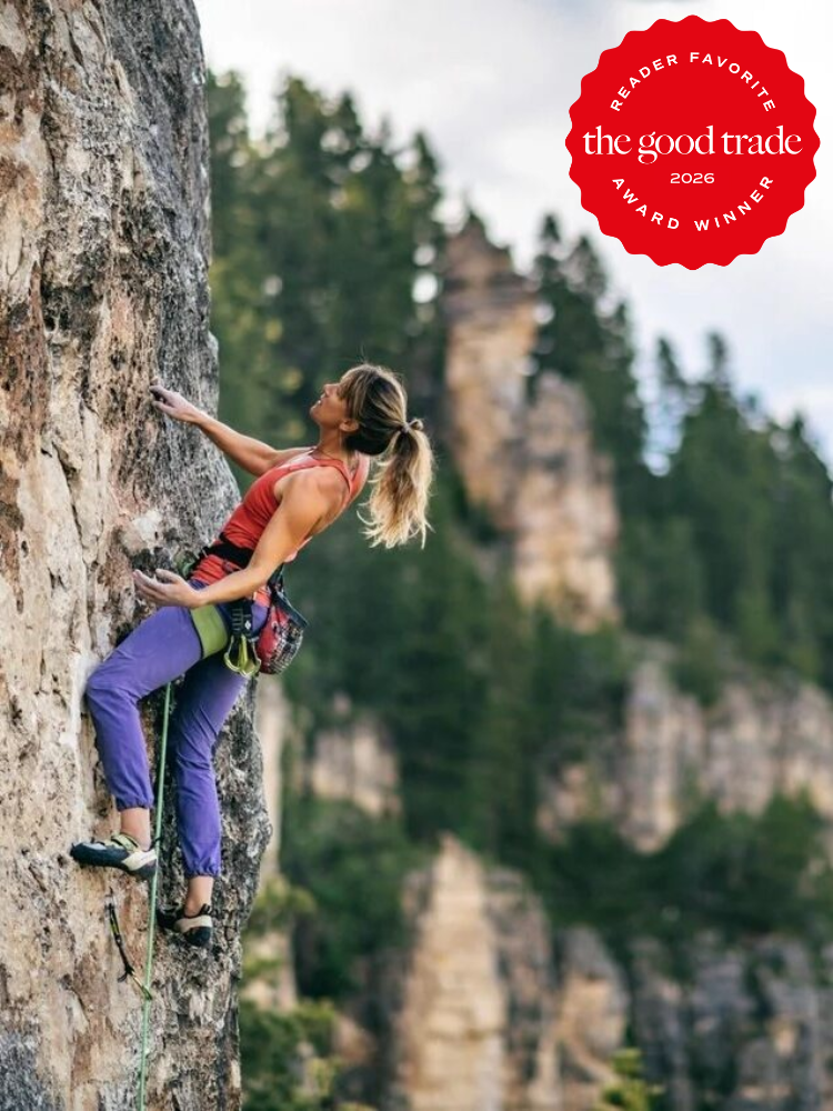 A woman in climbing gear ascends an outdoor rock face with a forested landscape in the background. A red “Reader Favorite” award badge from The Good Trade is in the top right corner.