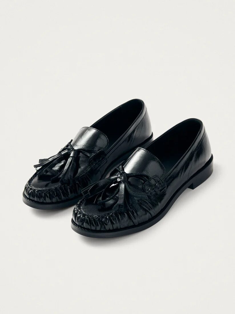 Pair of glossy black leather loafers with tassels on the front, set against a plain white background.