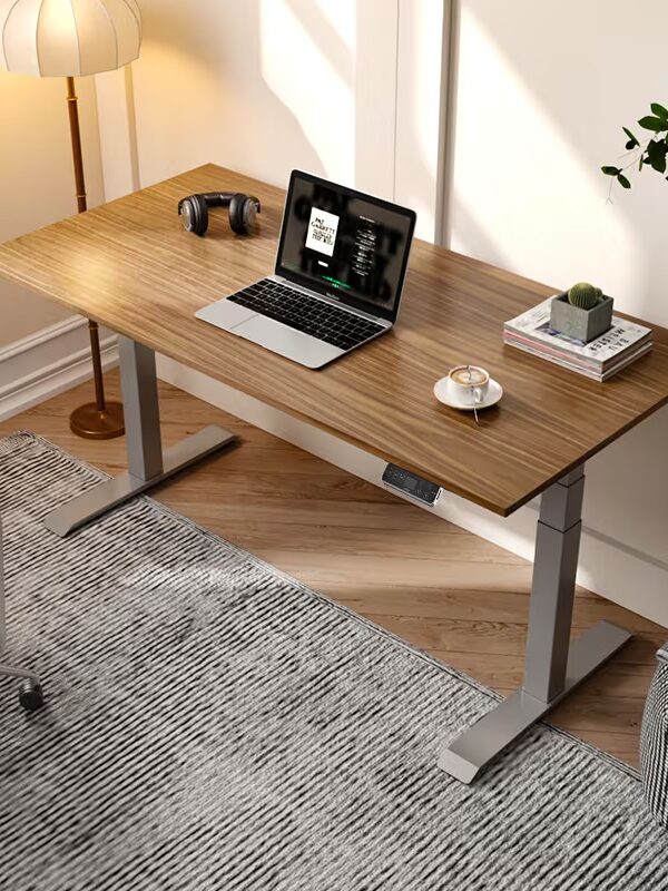A wooden desk with a laptop, headphones, a small plant, and a cup on it. A chair, floor lamp, and plant are nearby. The room has a carpet and sunlight from a window.