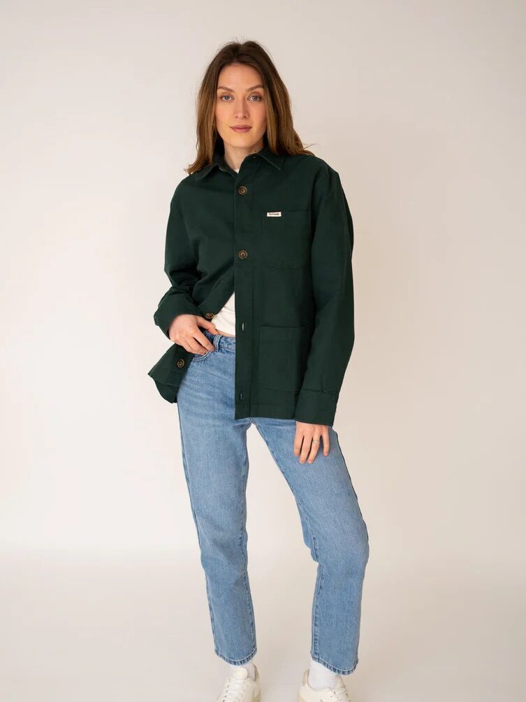 Person in a green jacket and blue jeans poses against a plain background.
