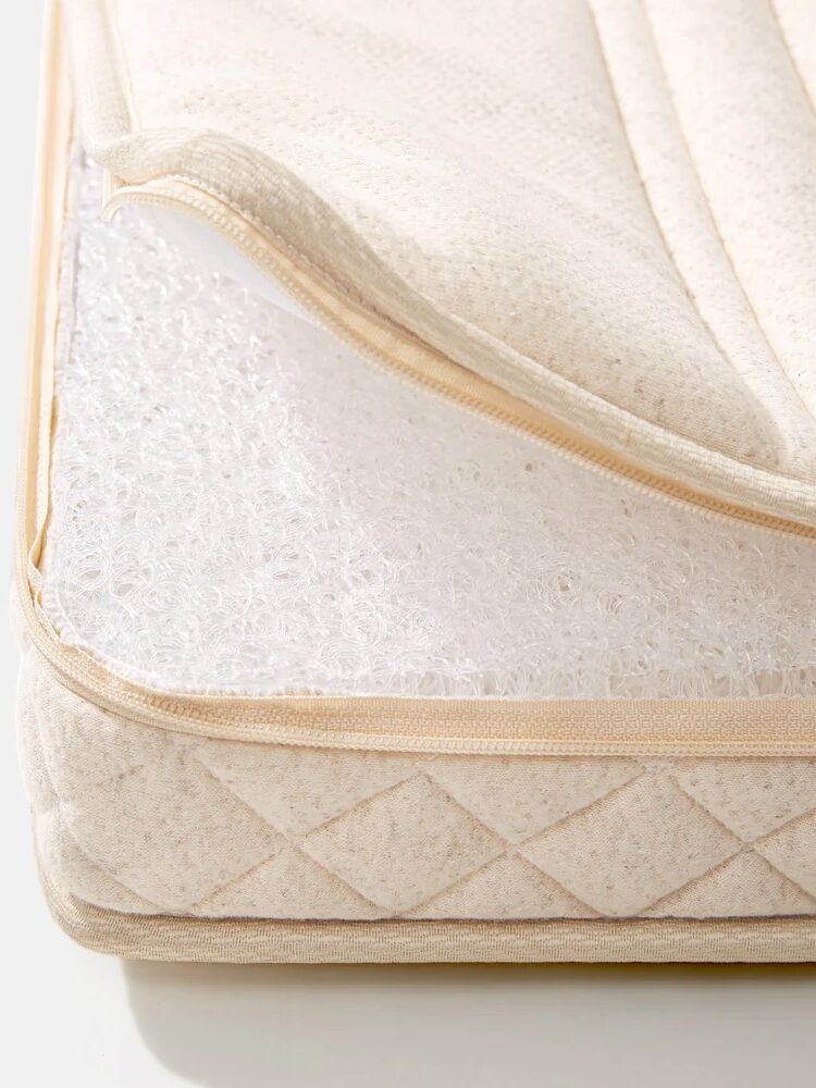 Close-up of a mattress corner with a partially unzipped beige fabric cover, revealing a white inner layer with a textured, fibrous material.