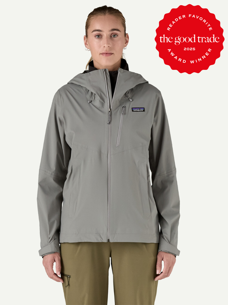 A person wearing a gray hooded Patagonia waterproof raincoat and olive pants stands facing forward. A red "The Good Trade Award Winner 2025" badge is in the top right corner.