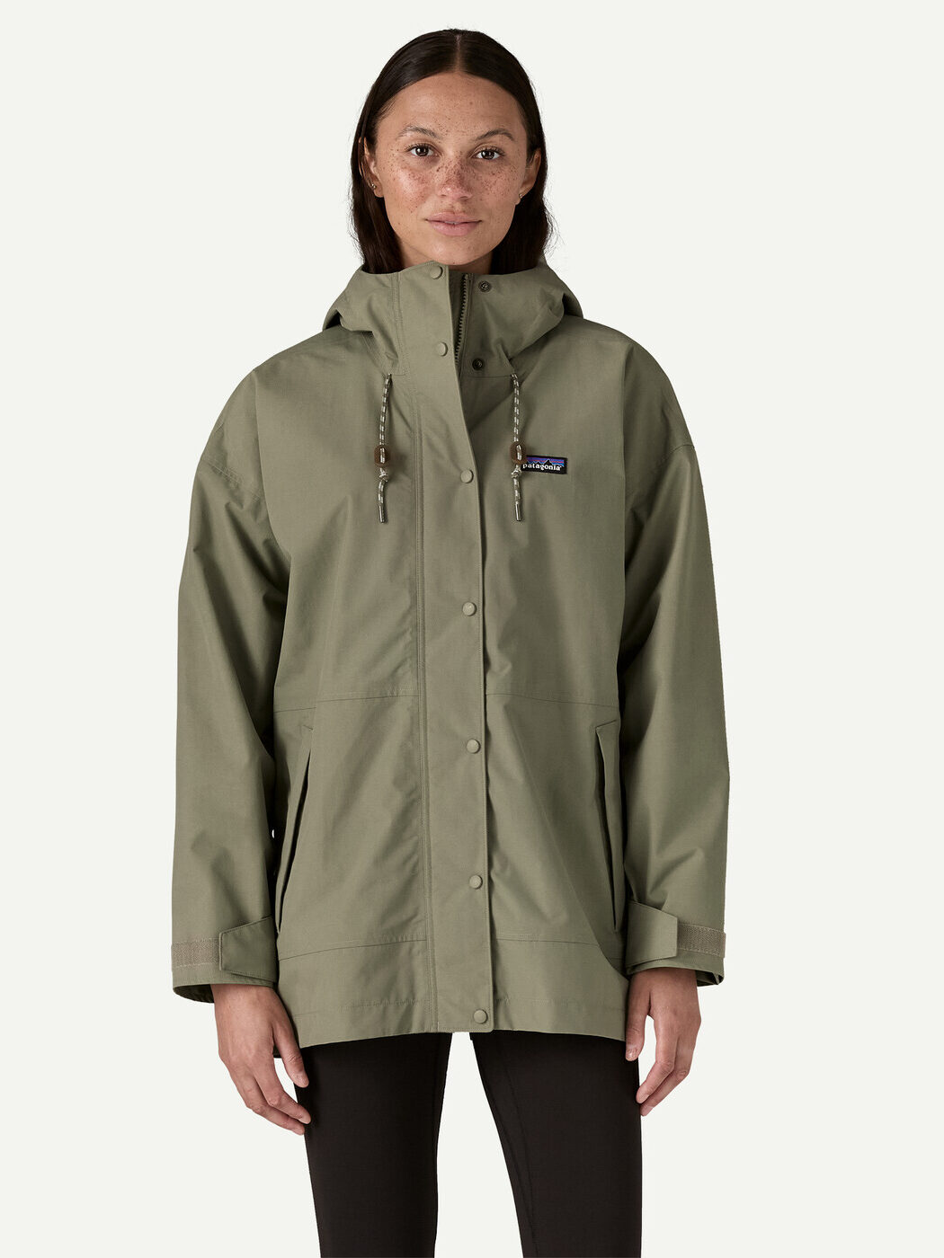 A person wearing an olive green hooded waterproof raincoat with a front zipper and snap buttons, standing against a plain light background.