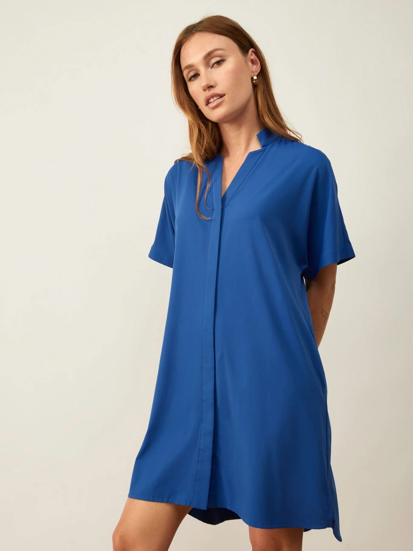 A woman wearing a loose-fitting, short-sleeved, knee-length royal blue dress stands against a plain light background.