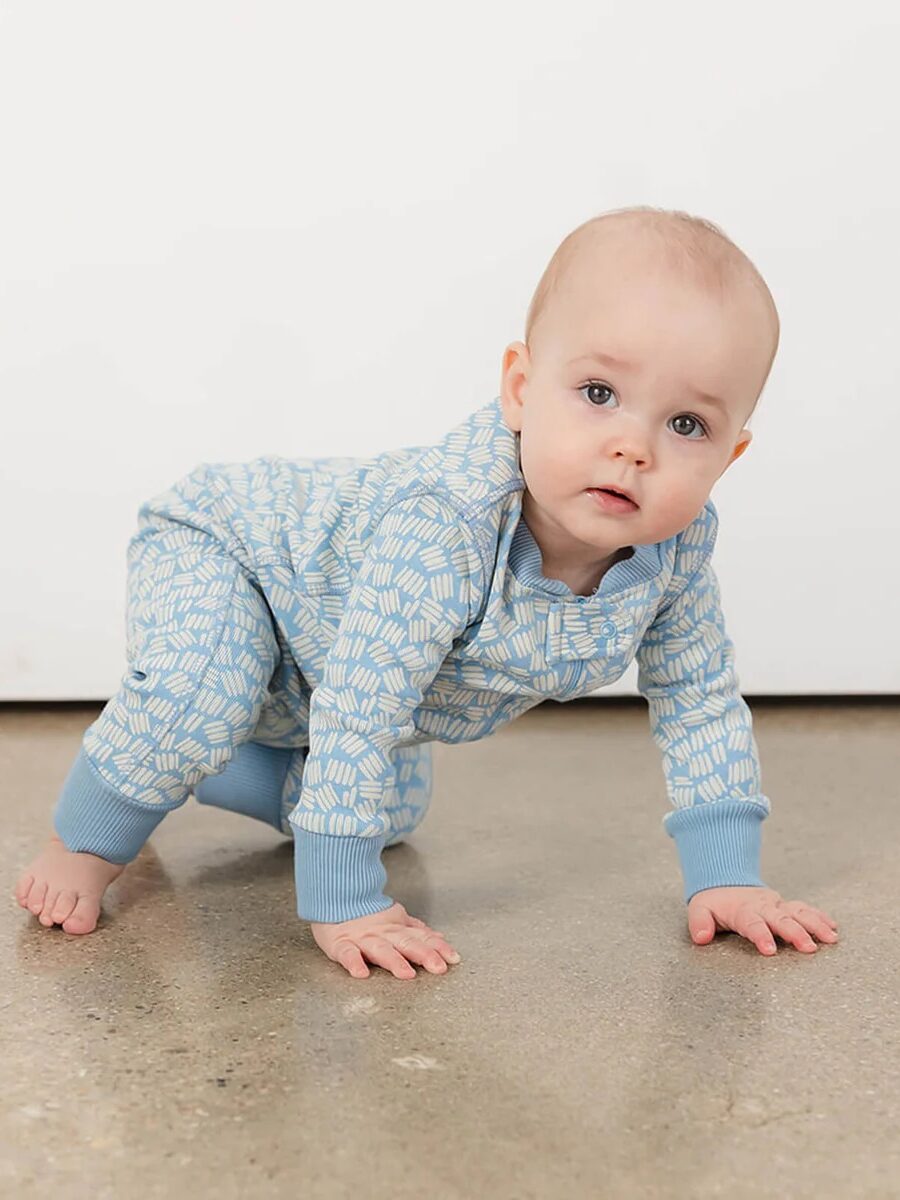 A baby wearing a blue patterned outfit is crawling on a polished concrete floor against a plain white background.