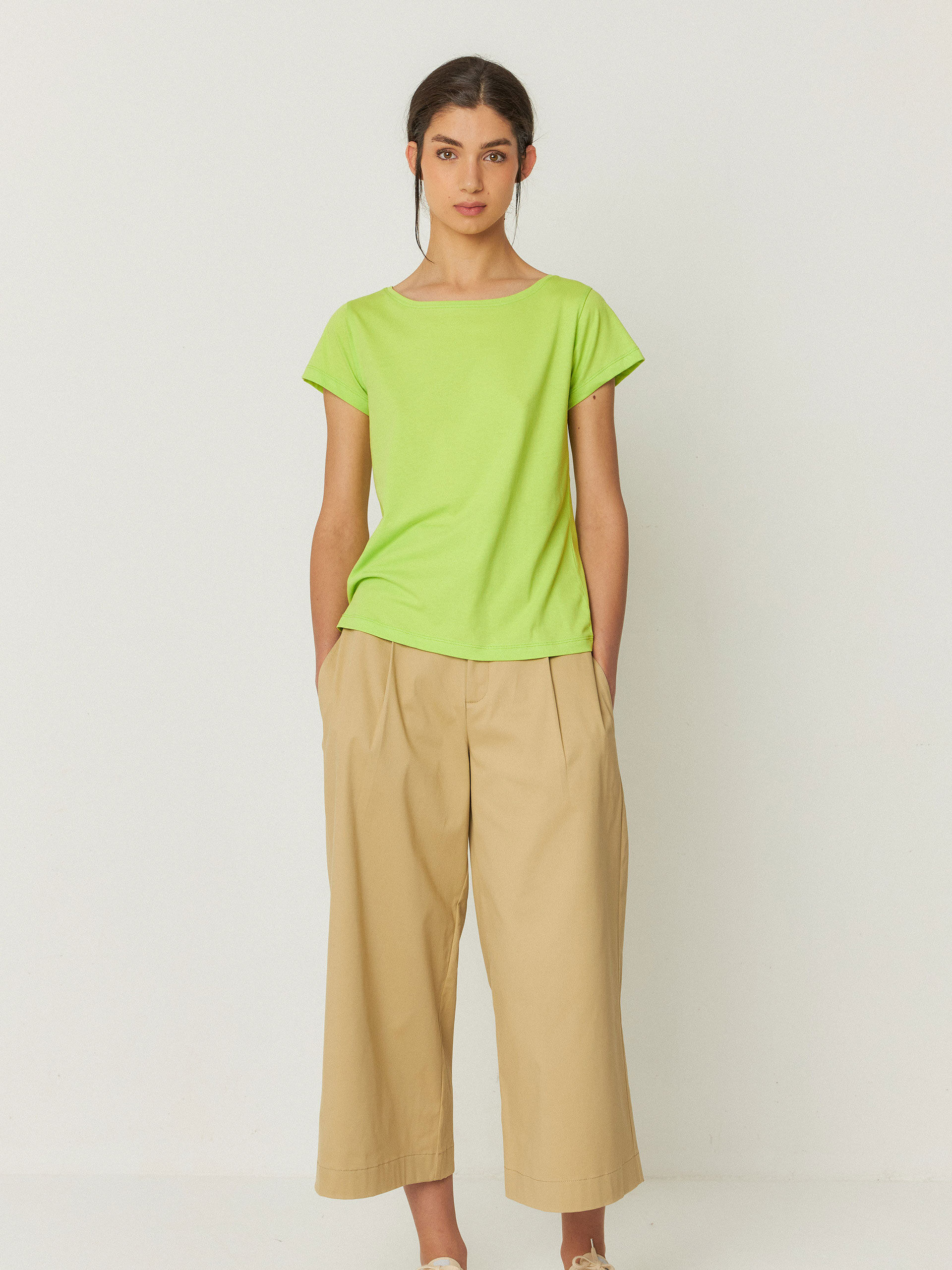 A person stands facing forward wearing a lime green short-sleeve t-shirt, beige wide-leg pants, and tan sneakers against a plain light background.