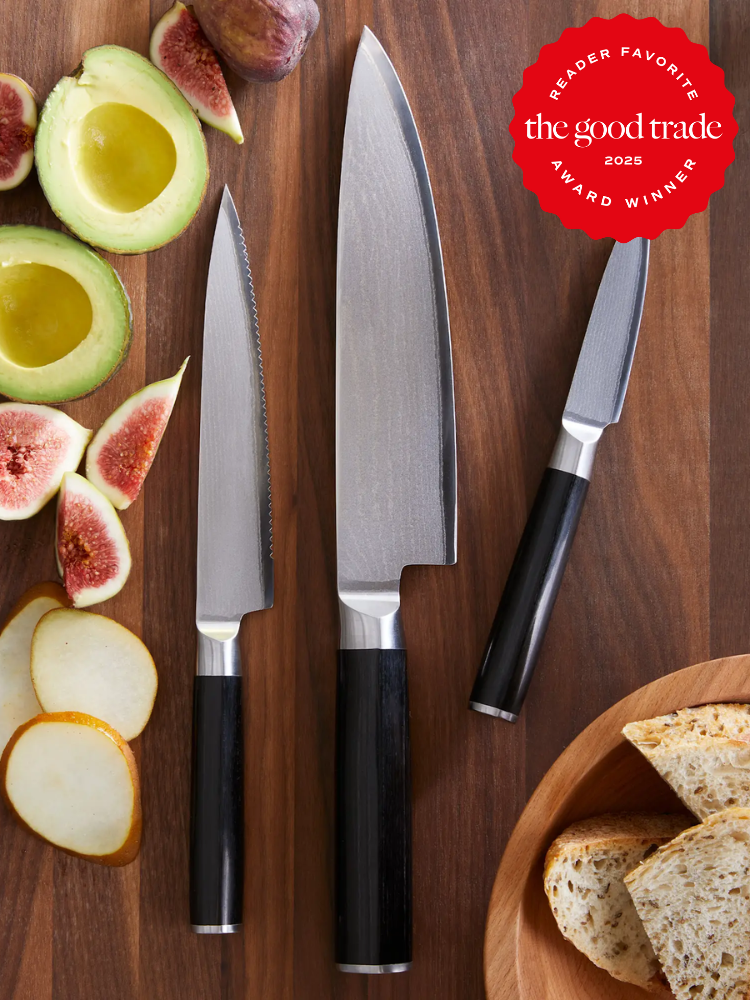 Three kitchen knives are arranged on a wooden surface with sliced avocado, figs, pear, and bread. A “Reader Favorite: The Good Trade 2025 Award Winner” badge is displayed at the top right.