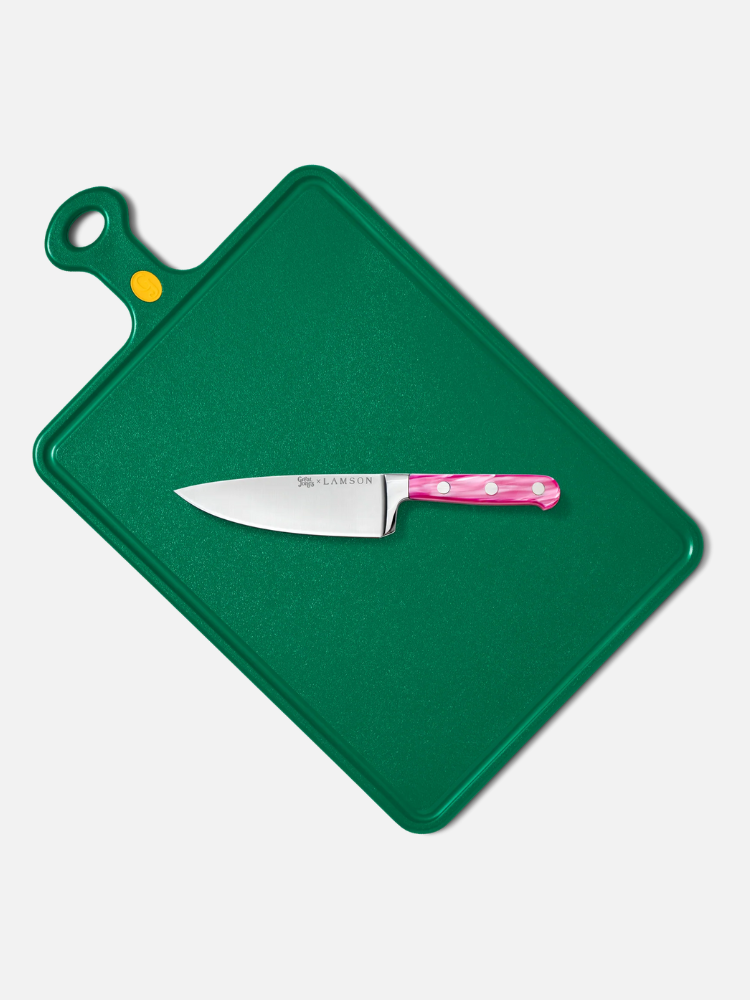 A green rectangular cutting board with a small chef’s knife featuring a pink handle with white polka dots resting on top.