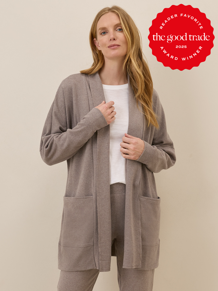 Woman wearing a taupe lounge set with a white shirt stands against a neutral background; a red "The Good Trade Award Winner 2023" badge appears in the upper right corner.