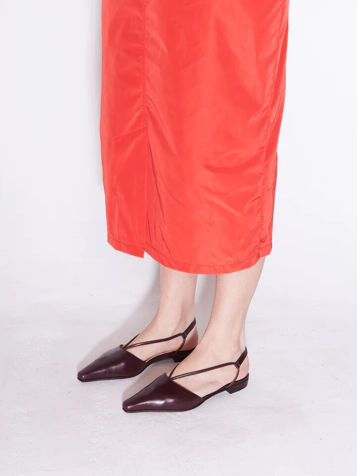 Person wearing a bright orange skirt and dark brown pointed slingback flats, standing on a light surface.