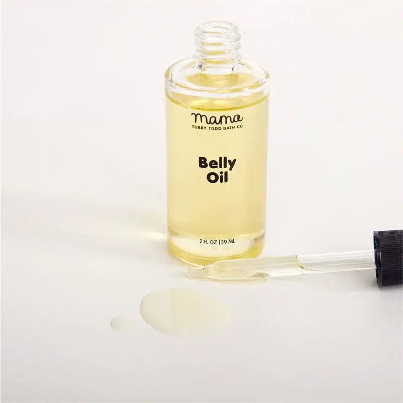 A clear bottle labeled "Belly Oil" with a dropper and some oil spilled on a white surface.