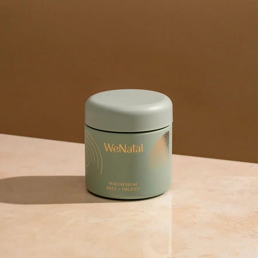 A green container labeled "WeNatal Magnesium Rest + Digest" sits on a beige surface with a neutral background.