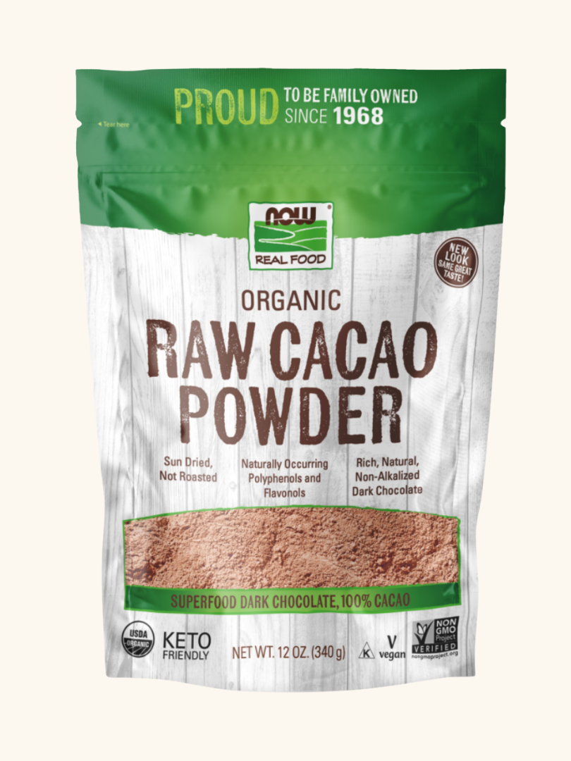 A 12 oz bag of NOW Real Food Organic Raw Cacao Powder with labeling highlighting features like "sun dried," "superfood," "keto friendly," and "vegan.