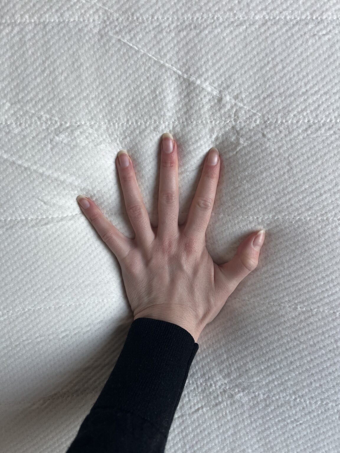 A hand pressing down on a white textured latex mattress surface, creating visible indentations.
