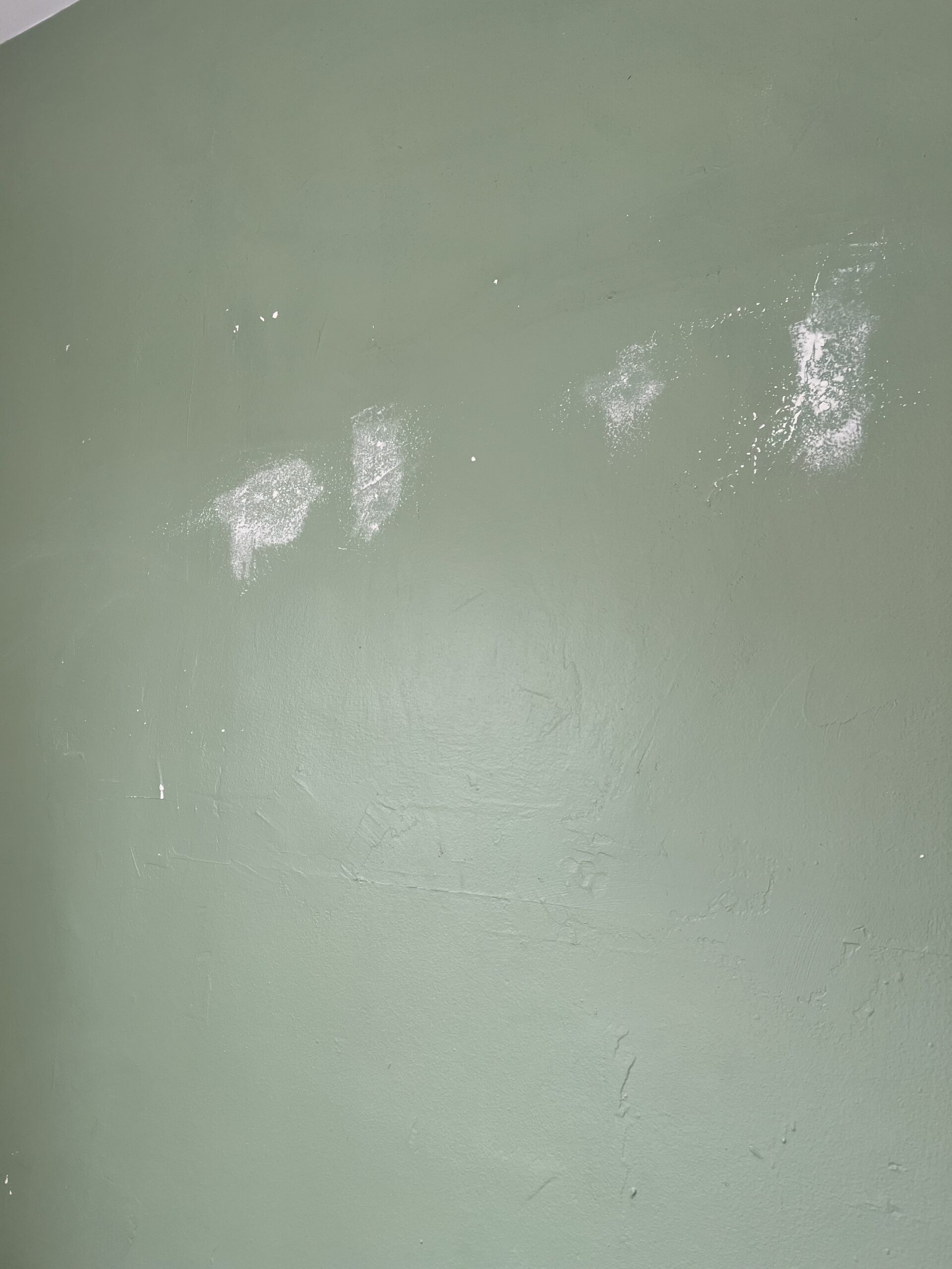 A green wall with several small white patches, possibly from recent repairs or spackling.