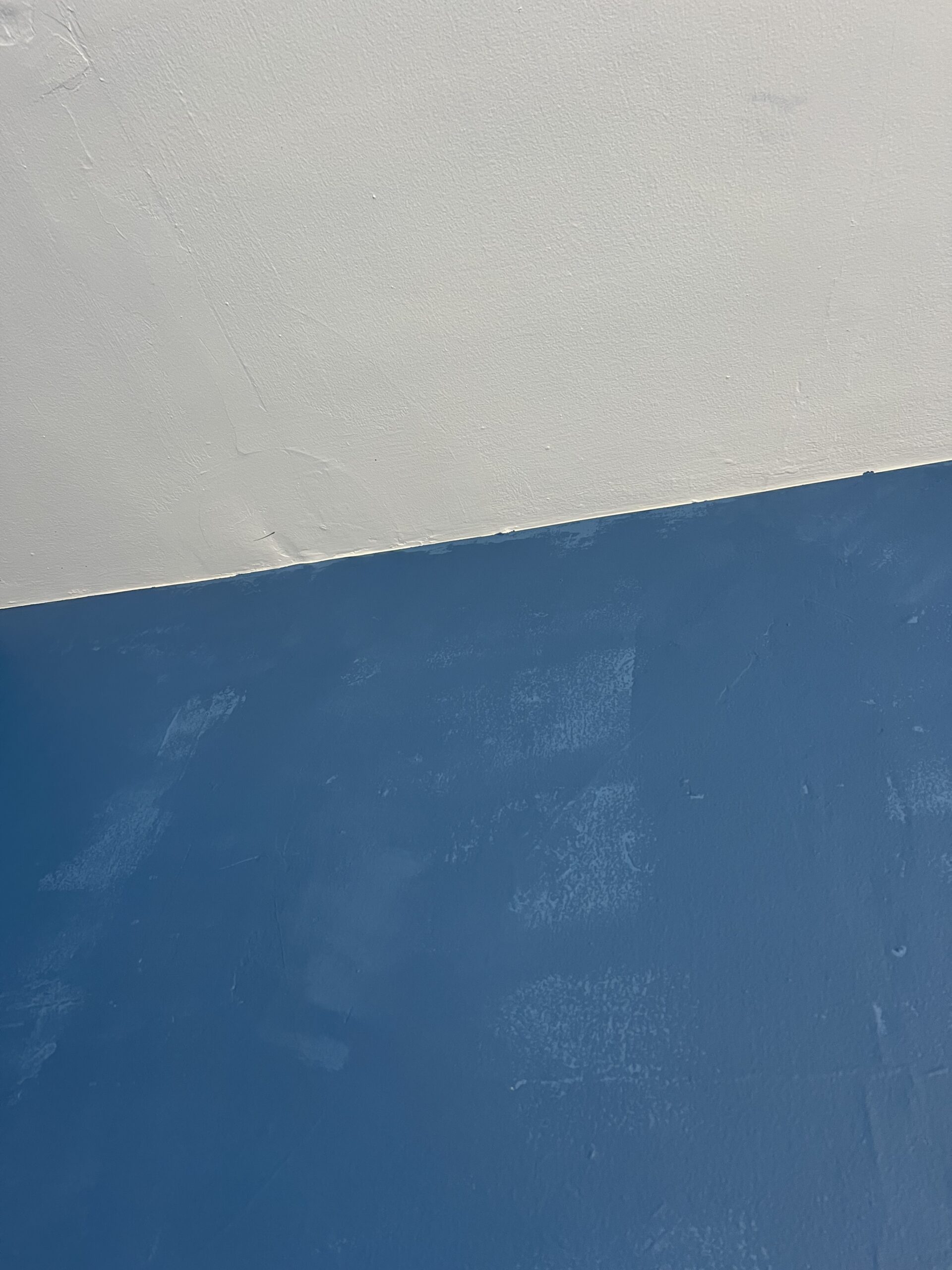 A wall painted blue meets a ceiling painted white, with visible brush strokes and texture on both surfaces.