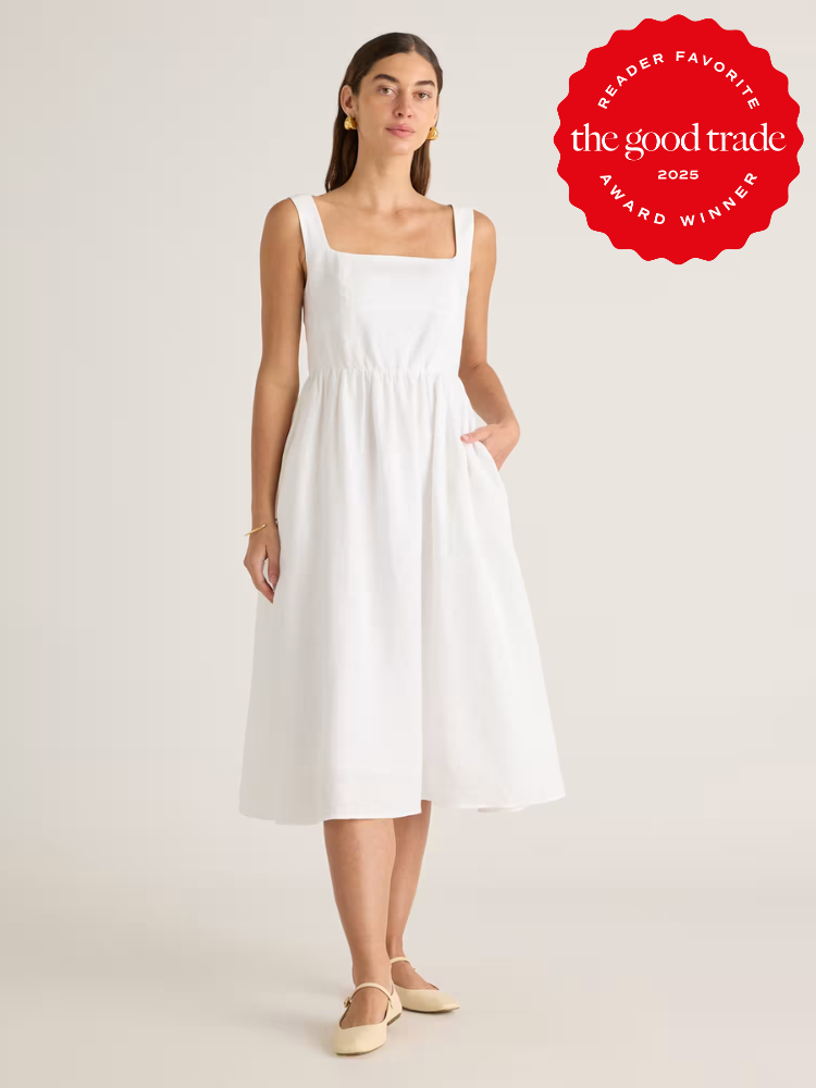 A woman wears a sleeveless, white, knee-length dress with a square neckline and pockets, standing against a plain background. A red "The Good Trade Award Winner 2025" badge is in the corner.