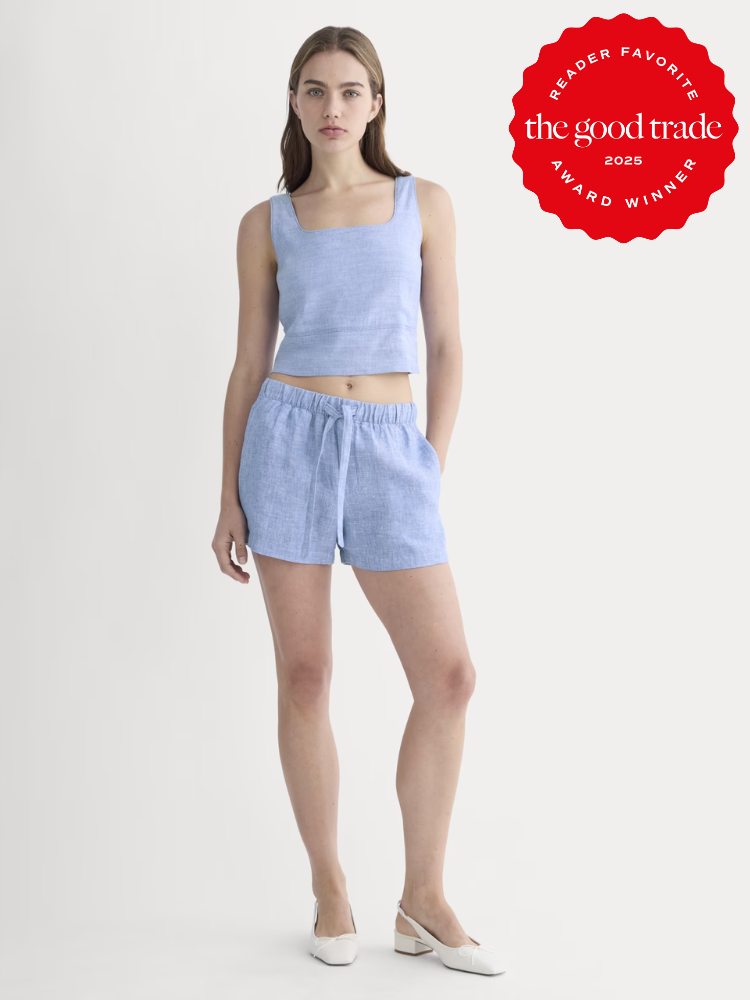 A woman wearing a light blue sleeveless crop top and matching shorts stands facing forward. A red "The Good Trade 2025 Award Winner" badge is displayed in the top right corner.