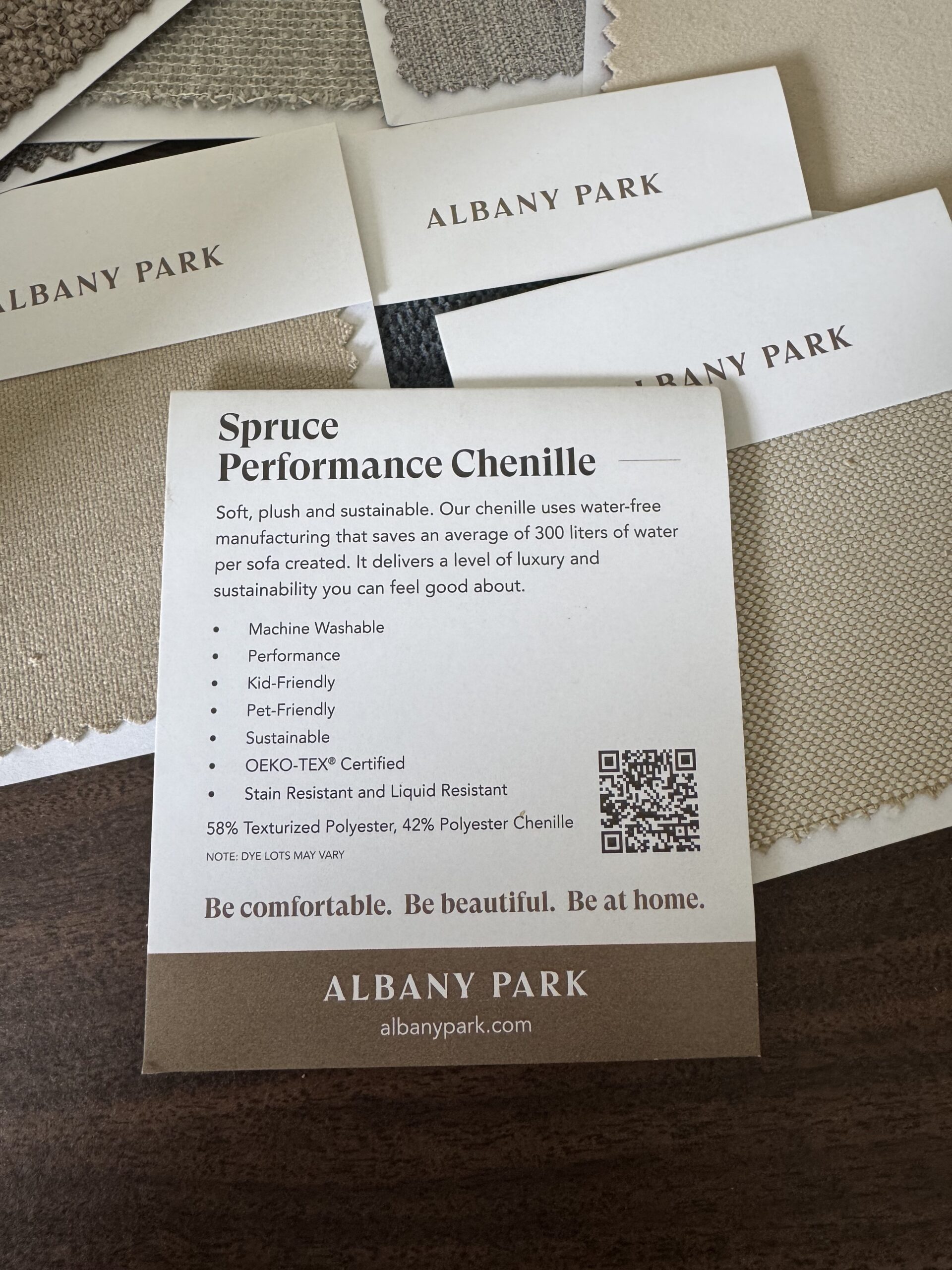 A card describes "Spruce Performance Chenille" fabric by Albany Park, listing features like machine washable, pet-friendly, and sustainable, with fabric swatches and business cards nearby.