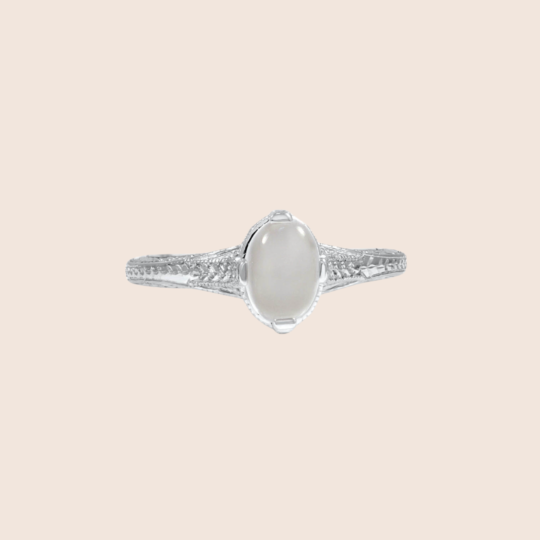A silver ring with an oval, translucent gemstone set in the center and an intricately detailed band, displayed on a plain light background.