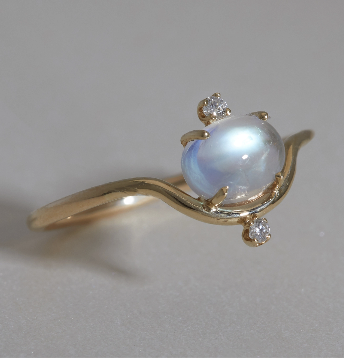 A gold ring featuring a round moonstone center, accented with three small round diamonds, displayed on a neutral surface.