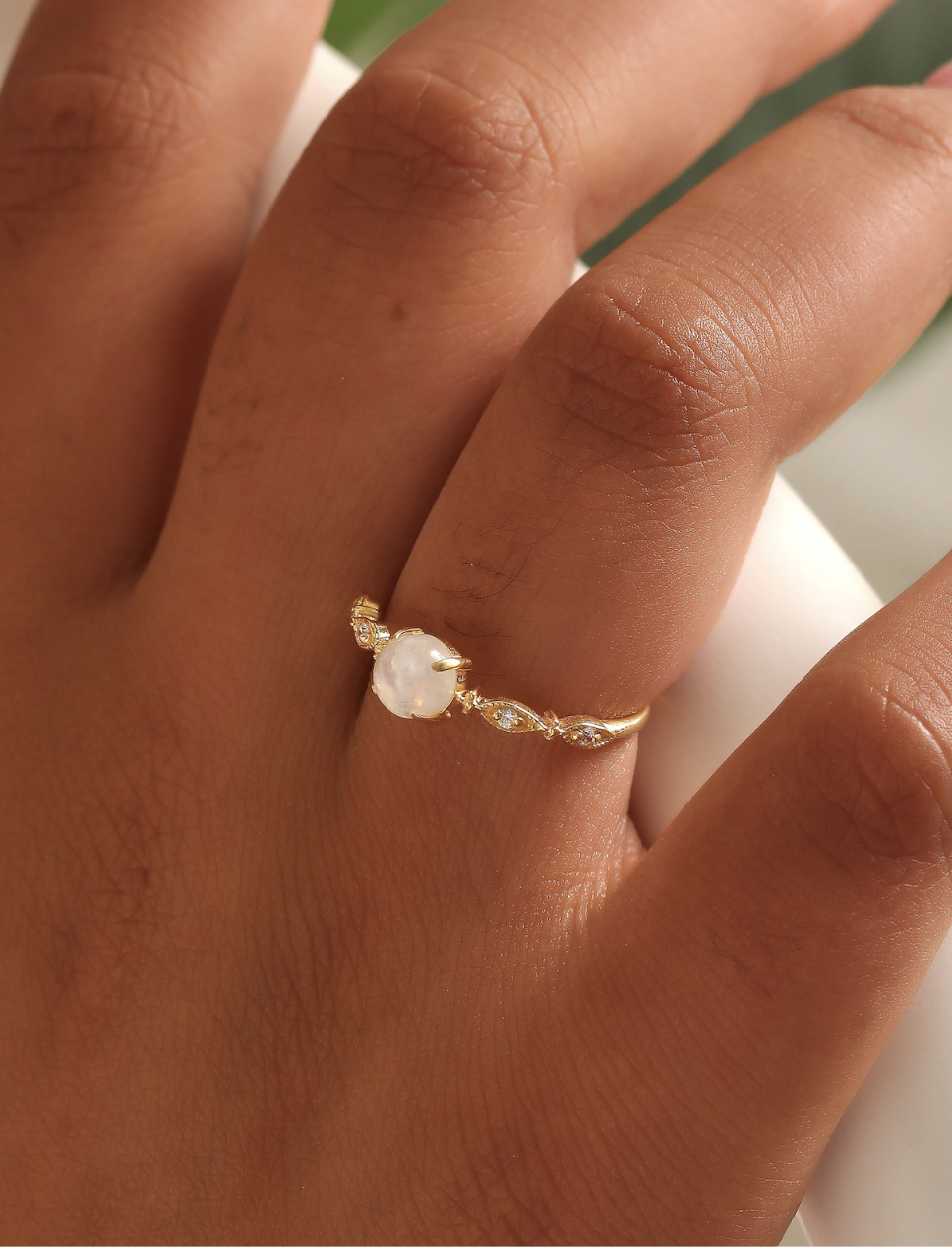 A hand wearing a gold ring with a round white gemstone center and two marquise-shaped accents on either side.