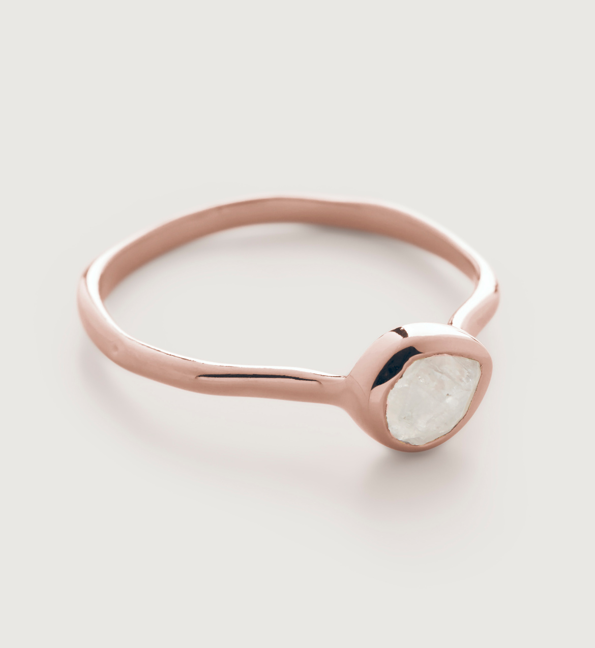 A rose gold ring with a rough, uncut white stone set in a simple, polished band, displayed on a light background.