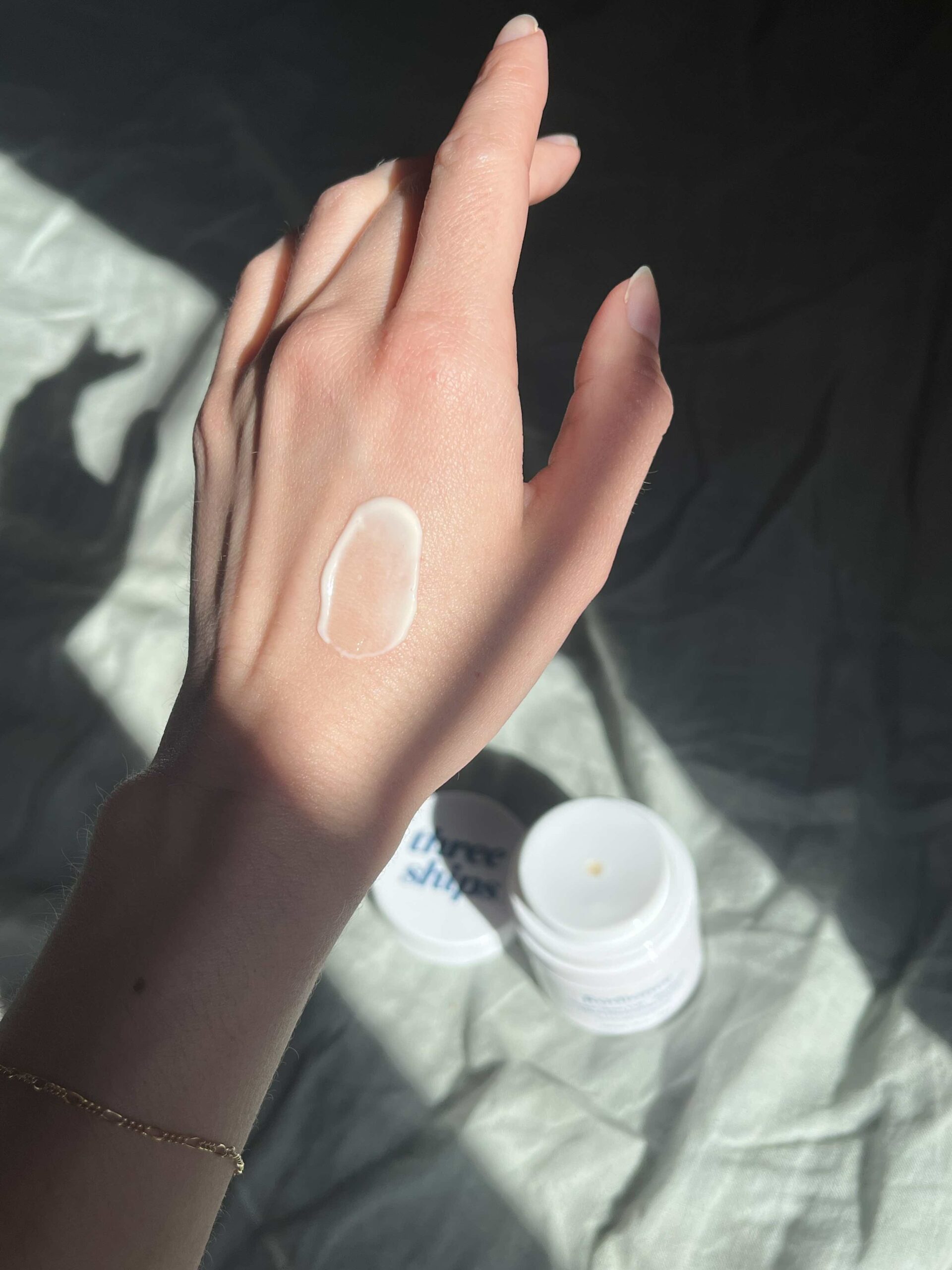 A hand with a swatch of cream on the back is shown in sunlight, with an open jar of Three Ships cream visible in the background.