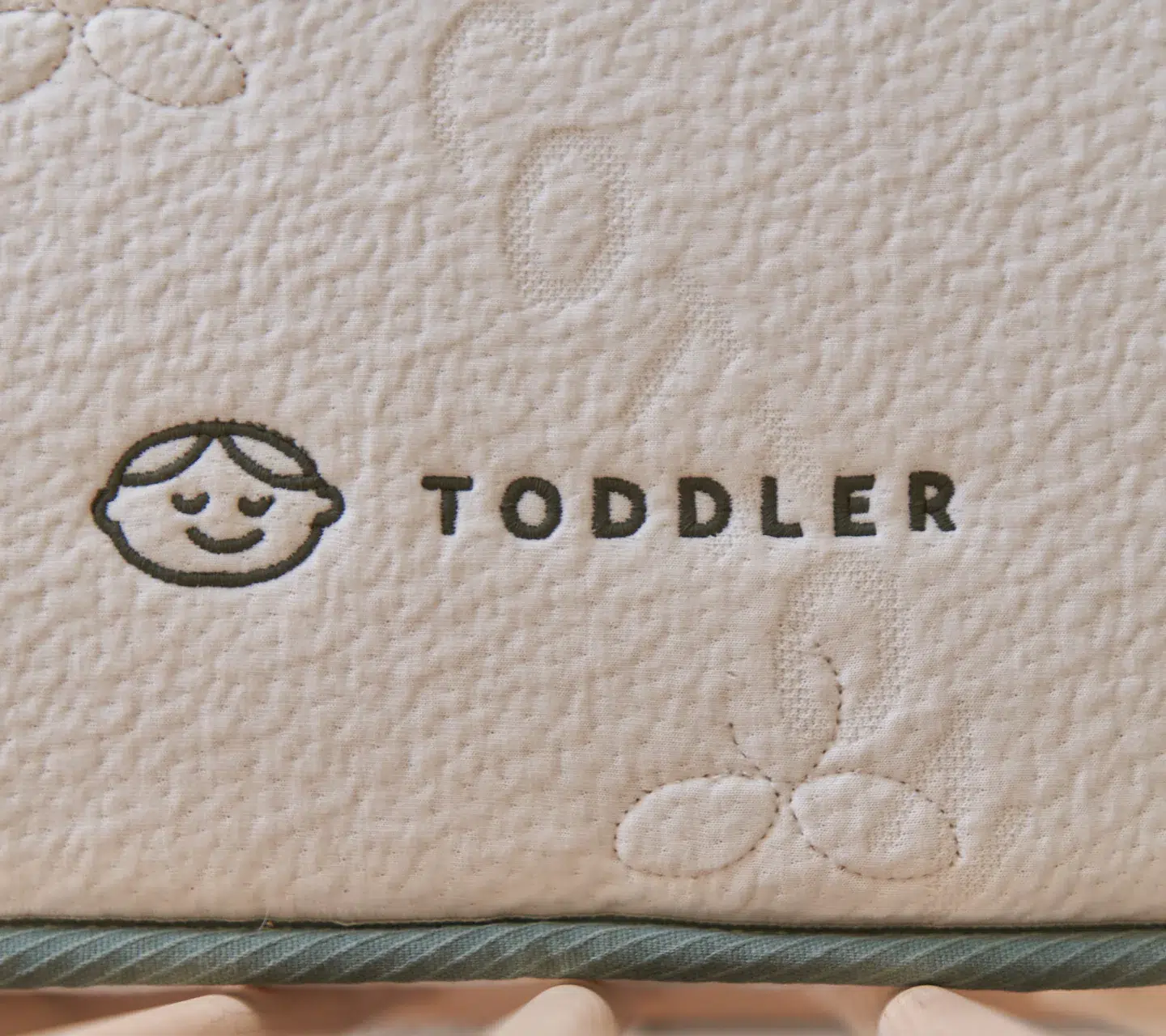 Close-up of a mattress label with a simple drawing of a child’s face and the word "TODDLER" stitched onto the fabric.