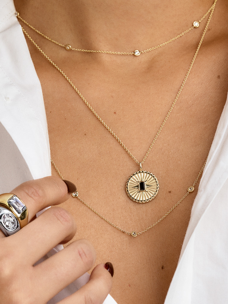 A person wearing a white shirt, layered gold necklaces with a pendant, and several silver and gold rings on one hand.