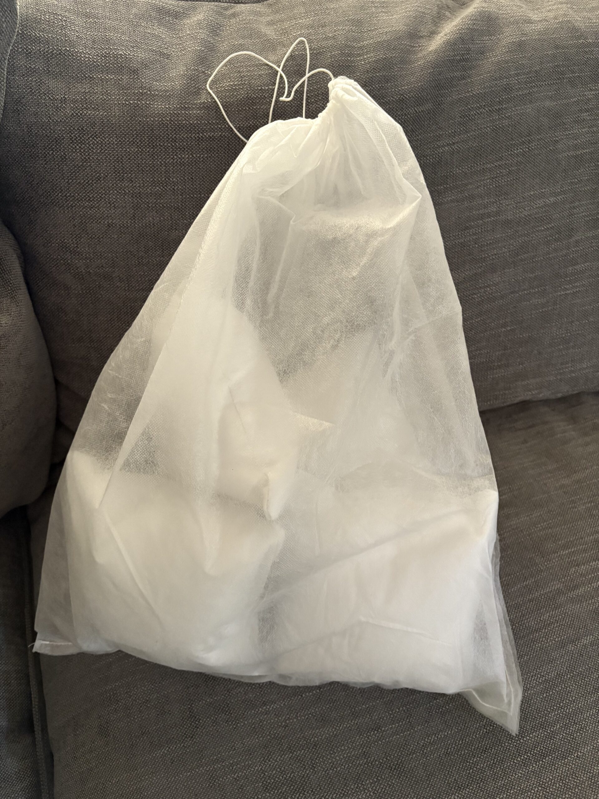 A white mesh drawstring bag containing several white items, placed on a gray fabric couch.