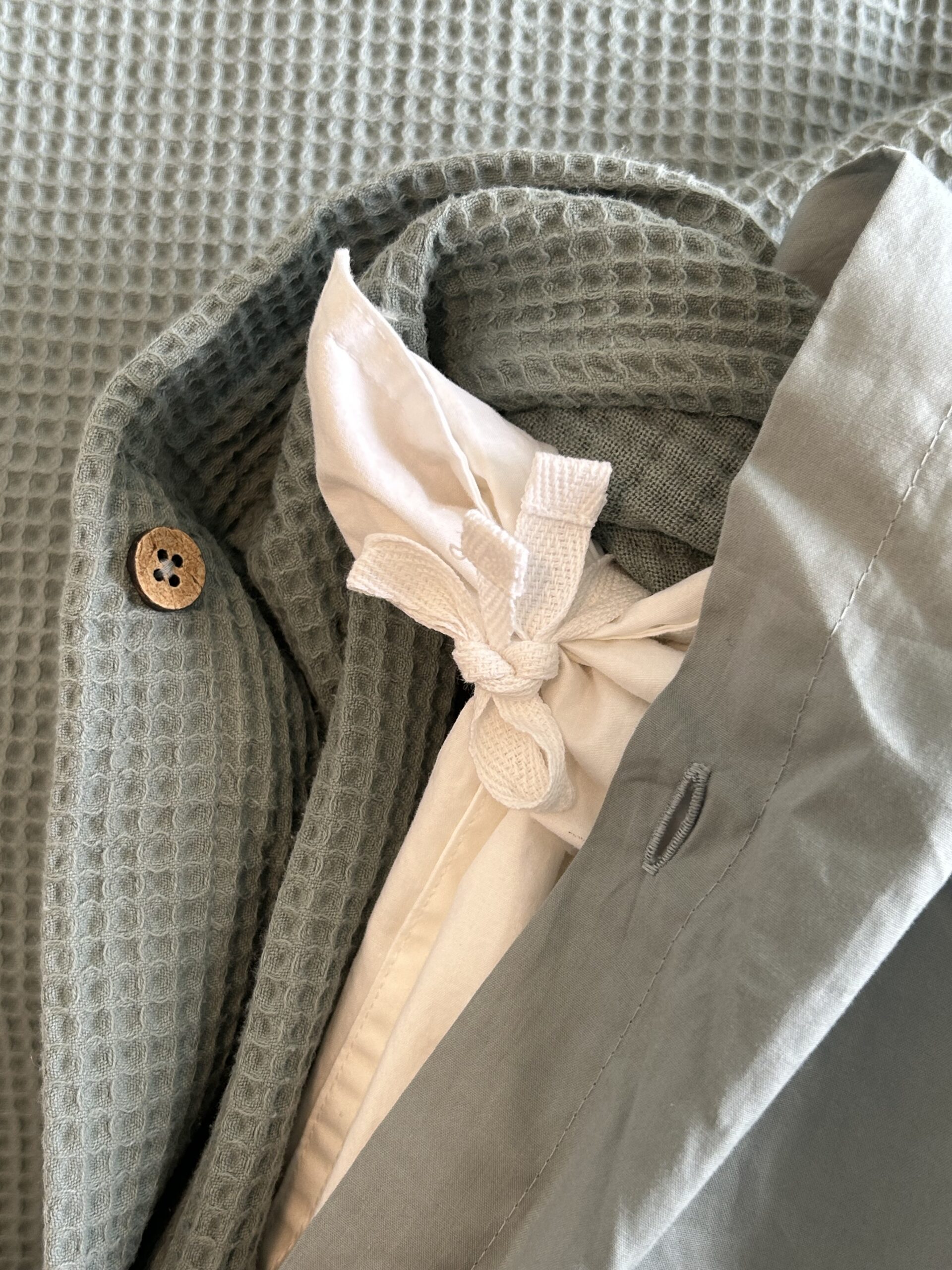 A close-up of a light green textured bathrobe with a brown button, a white belt tie, and a folded collar.