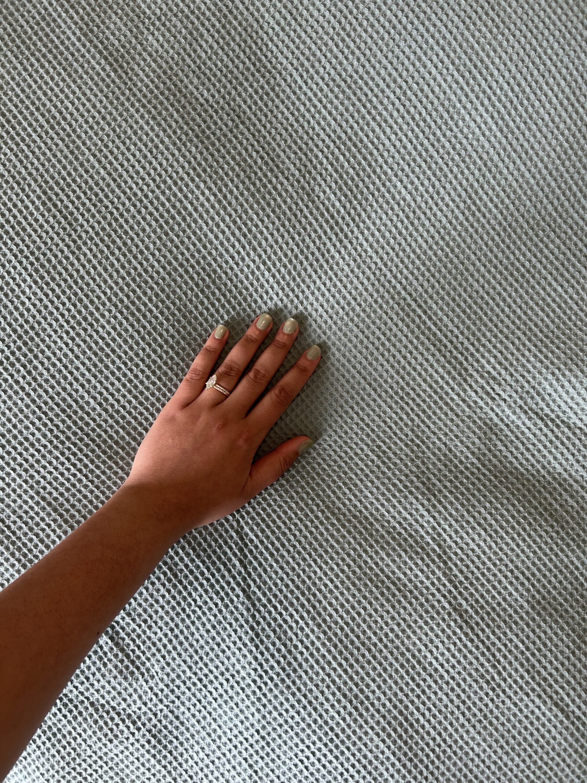A left hand with painted nails and a ring rests on a textured, light grey fabric surface.