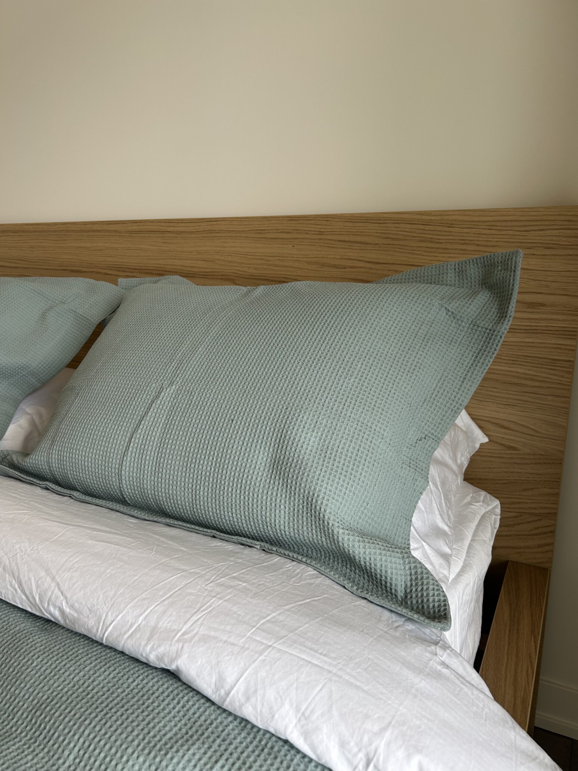 A neatly made bed with a wooden headboard, featuring light green textured pillowcases and bedding, with white sheets underneath.