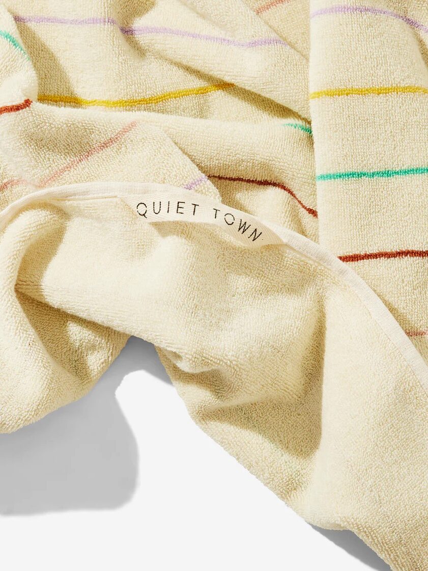 A cream-colored organic towel with thin, multicolored stripes and the words “QUIET TOWN” printed on the edge.