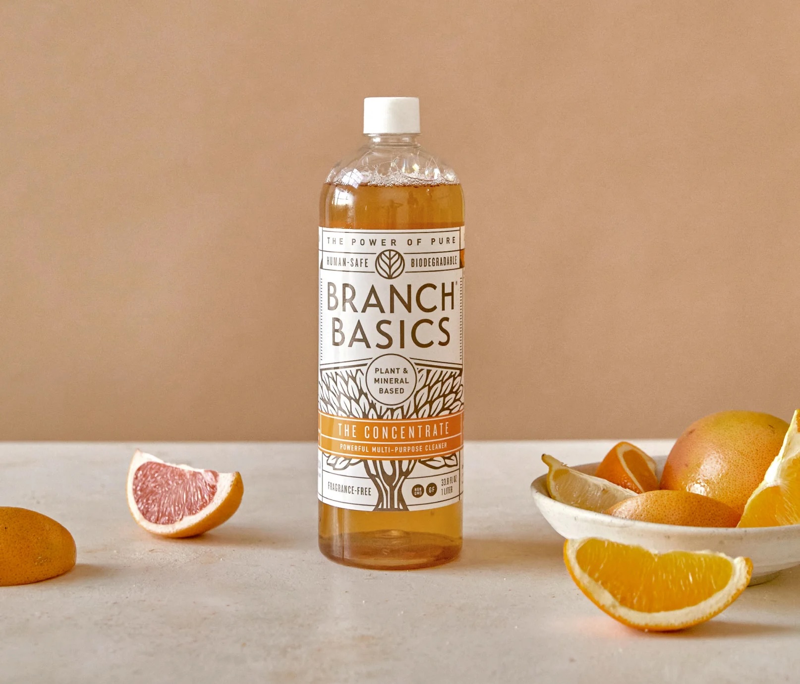 A bottle of Branch Basics cleaning concentrate is placed on a light surface next to sliced citrus fruits against a beige background.