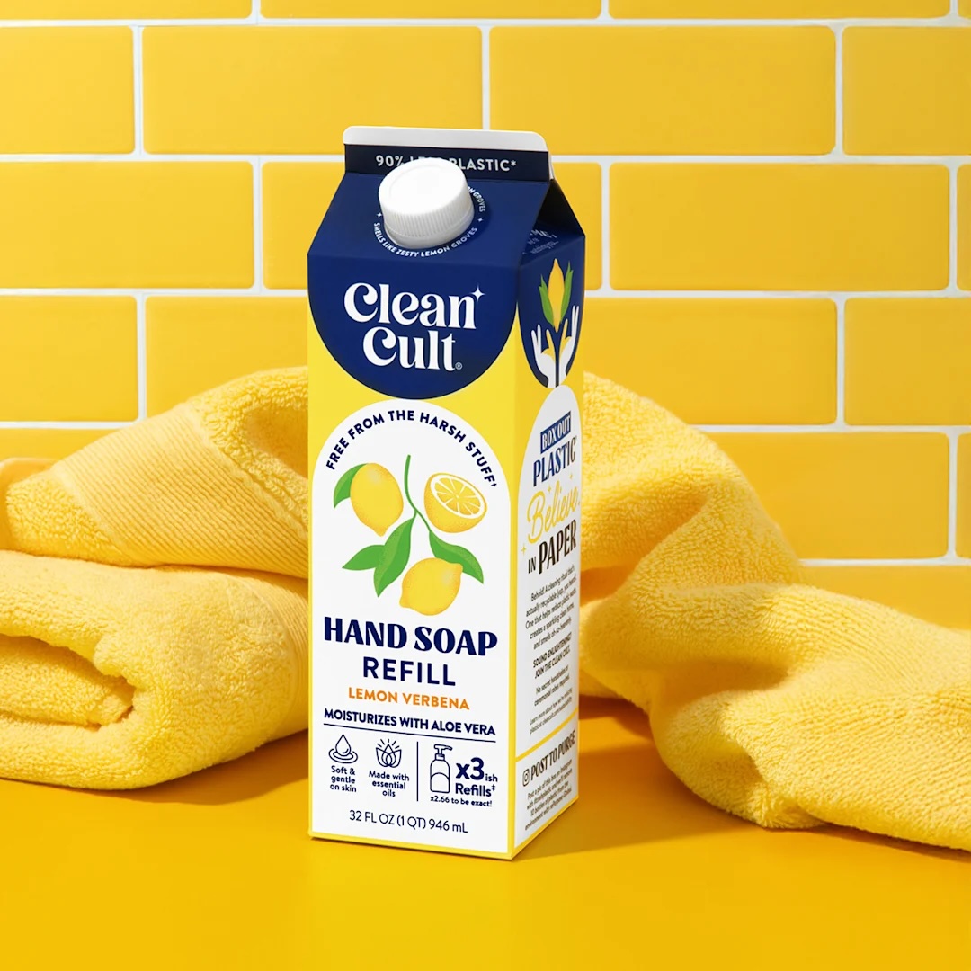 A carton of CleanCult Lemon Verbena Hand Soap Refill is placed on a yellow surface with a yellow towel and a yellow tiled wall in the background.