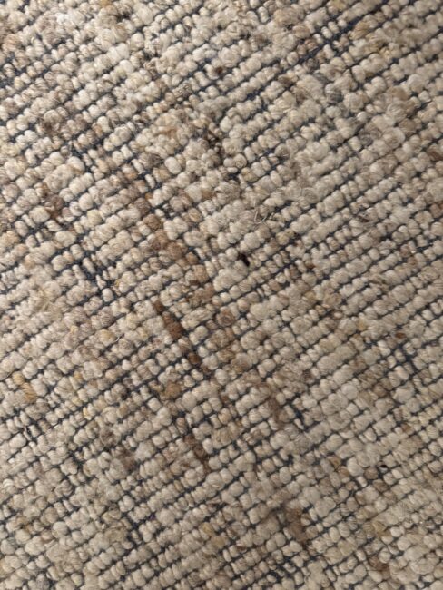 Close-up of a textured, woven fabric with a pattern of beige, brown, and gray threads in a grid-like arrangement.