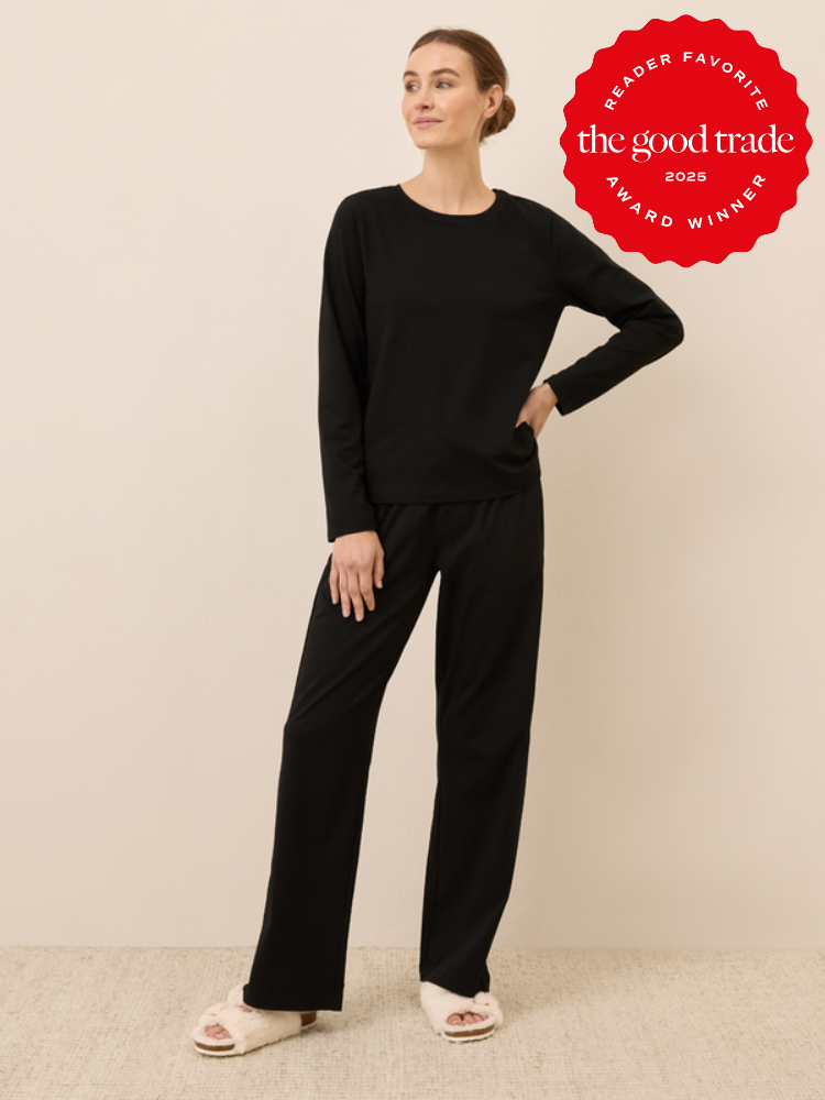 A woman stands against a neutral background wearing a black long-sleeve top, black pants, and white slippers. "The Good Trade 2025 Award Winner" badge is displayed in the top right corner.