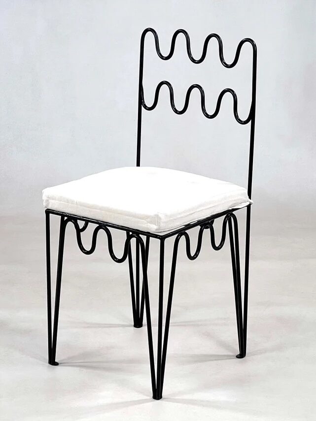 A black metal chair with a wavy, zigzag design on the backrest and seat frame, featuring a white cushioned seat. The Kesh Tiles logo is visible in the lower right corner.