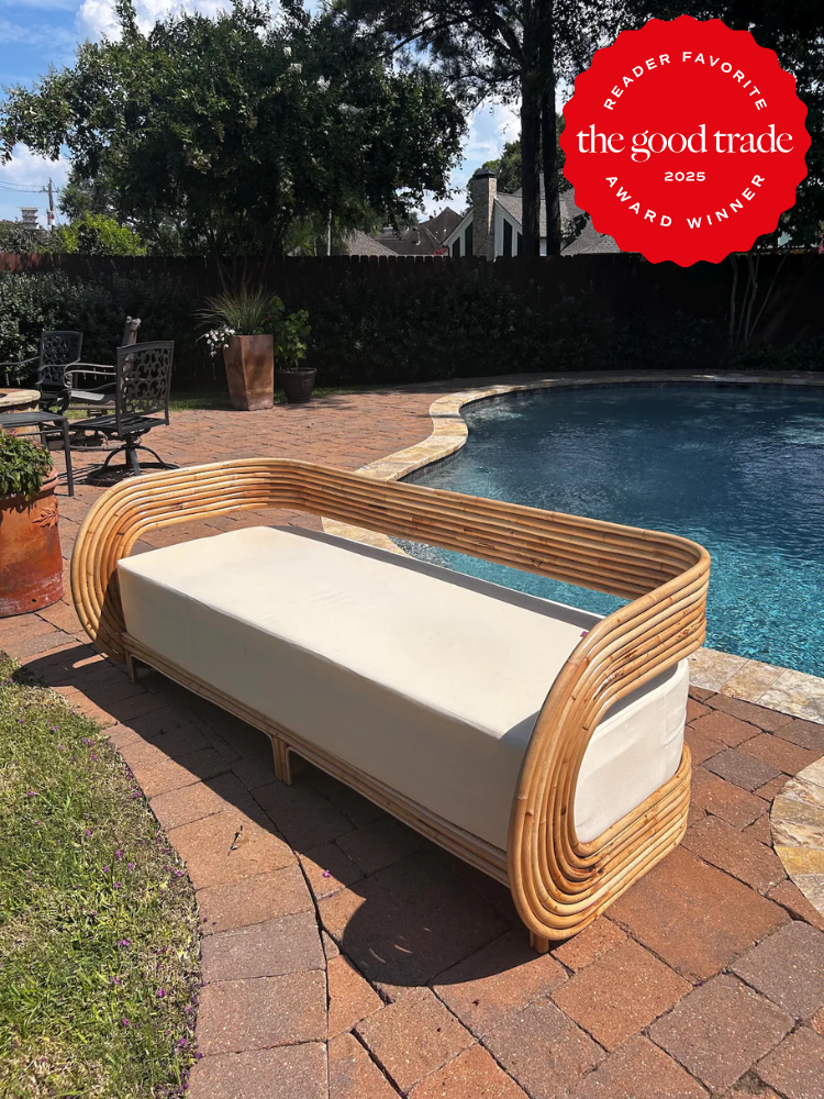A rattan outdoor sofa with a white cushion is placed on a brick patio beside a swimming pool; a red "The Good Trade 2025 Award Winner" badge is in the corner.