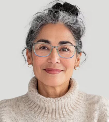 A middle-aged woman with gray hair tied back, wearing glasses, gold hoop earrings, and a light-colored turtleneck sweater, smiling at the camera against a plain background.