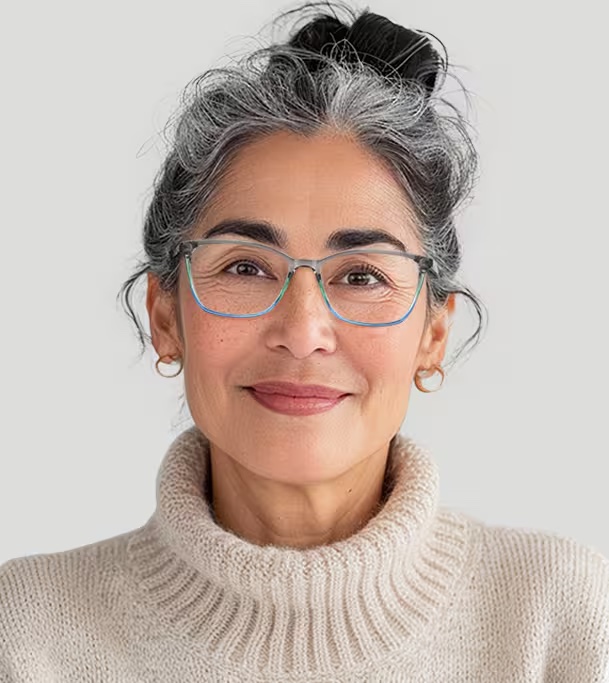 A middle-aged woman with gray hair tied back, wearing glasses, gold hoop earrings, and a light-colored turtleneck sweater, smiling at the camera against a plain background.