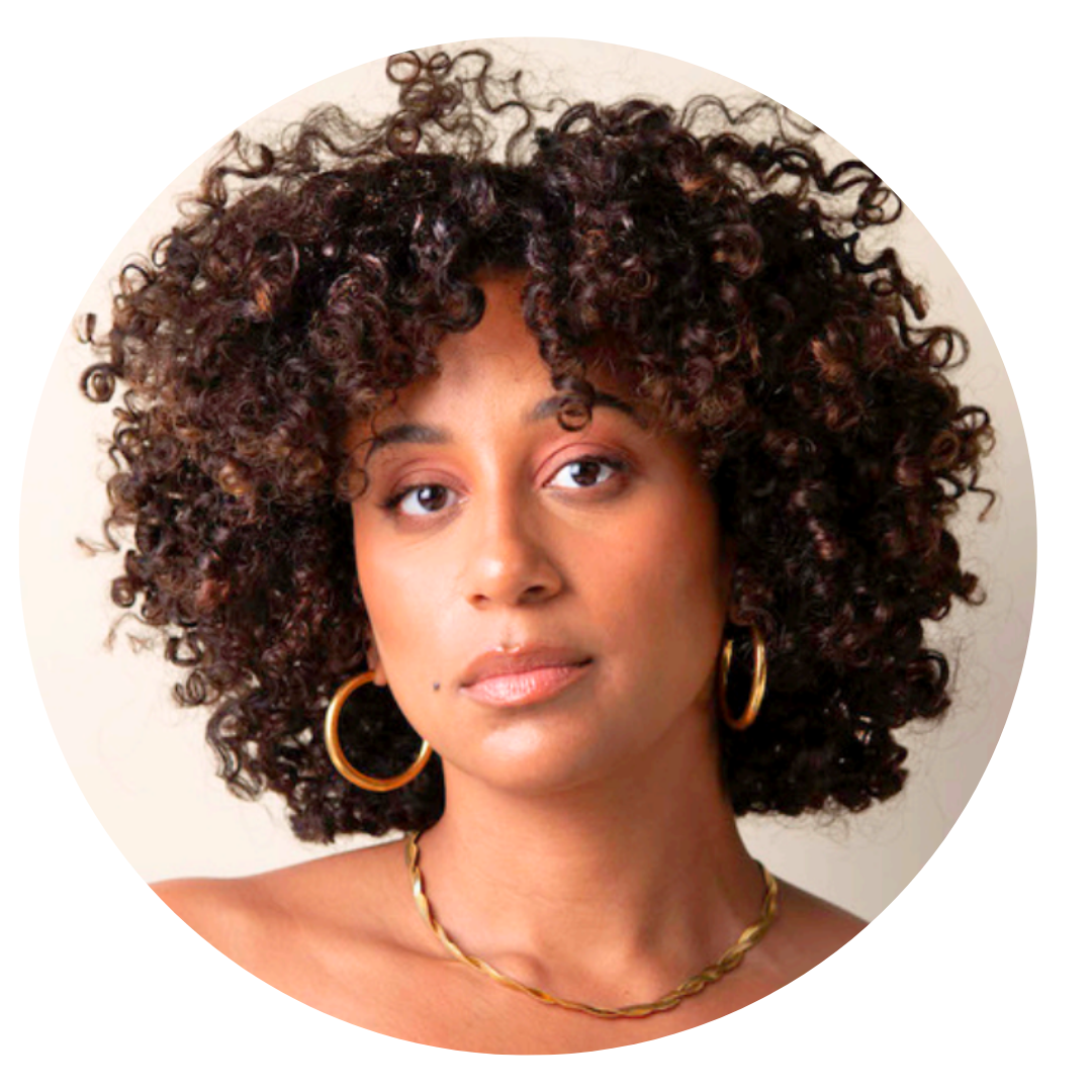 Woman with medium brown skin and curly dark brown hair, wearing large hoop earrings and a gold necklace, looks at the camera against a neutral background.