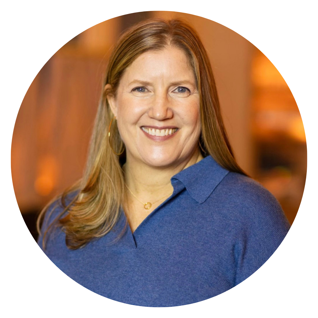A woman with long light brown hair, wearing a blue sweater and gold hoop earrings, smiles at the camera against a blurred warm-toned background.