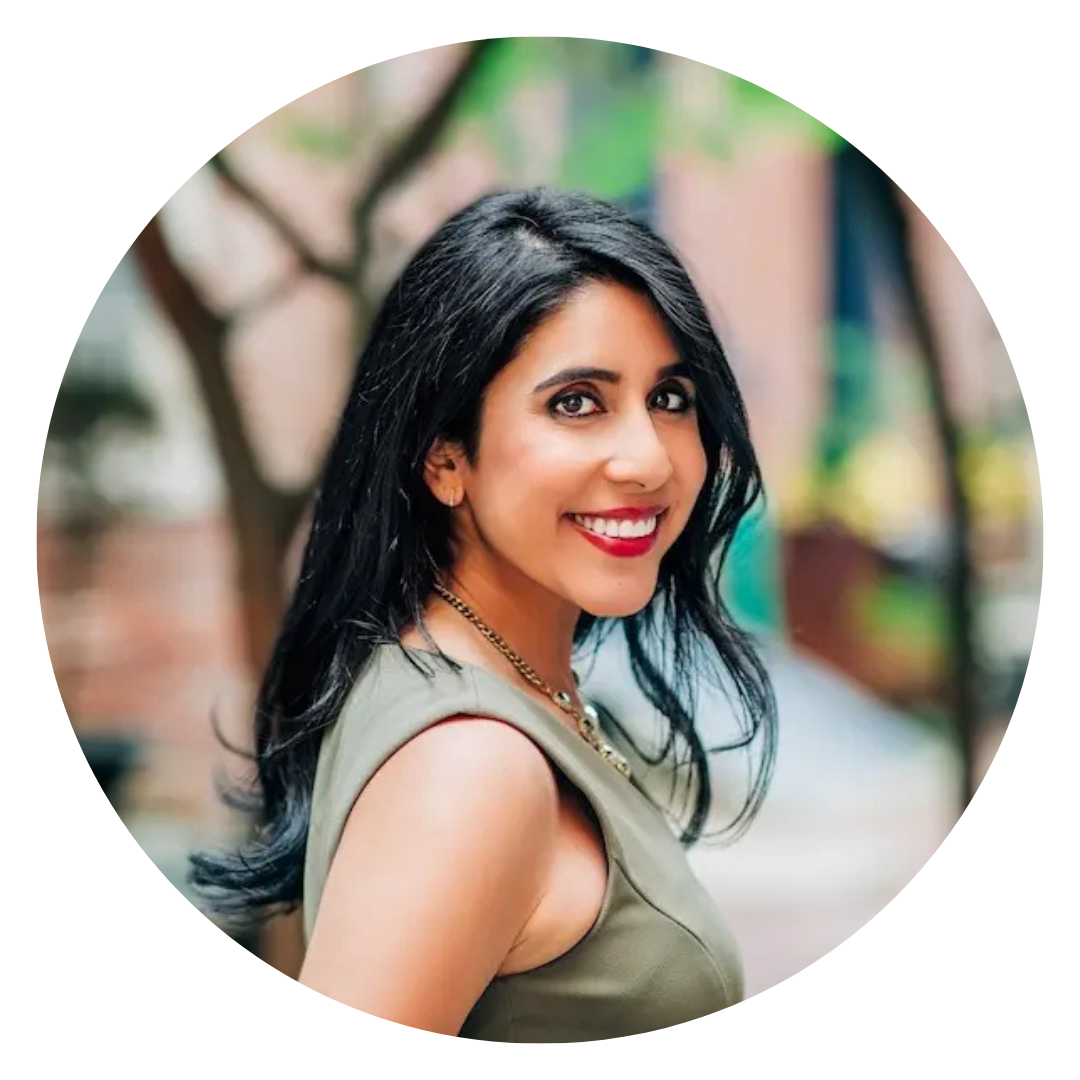 Woman with long dark hair and a sleeveless green top smiling outdoors, with blurred trees and buildings in the background.