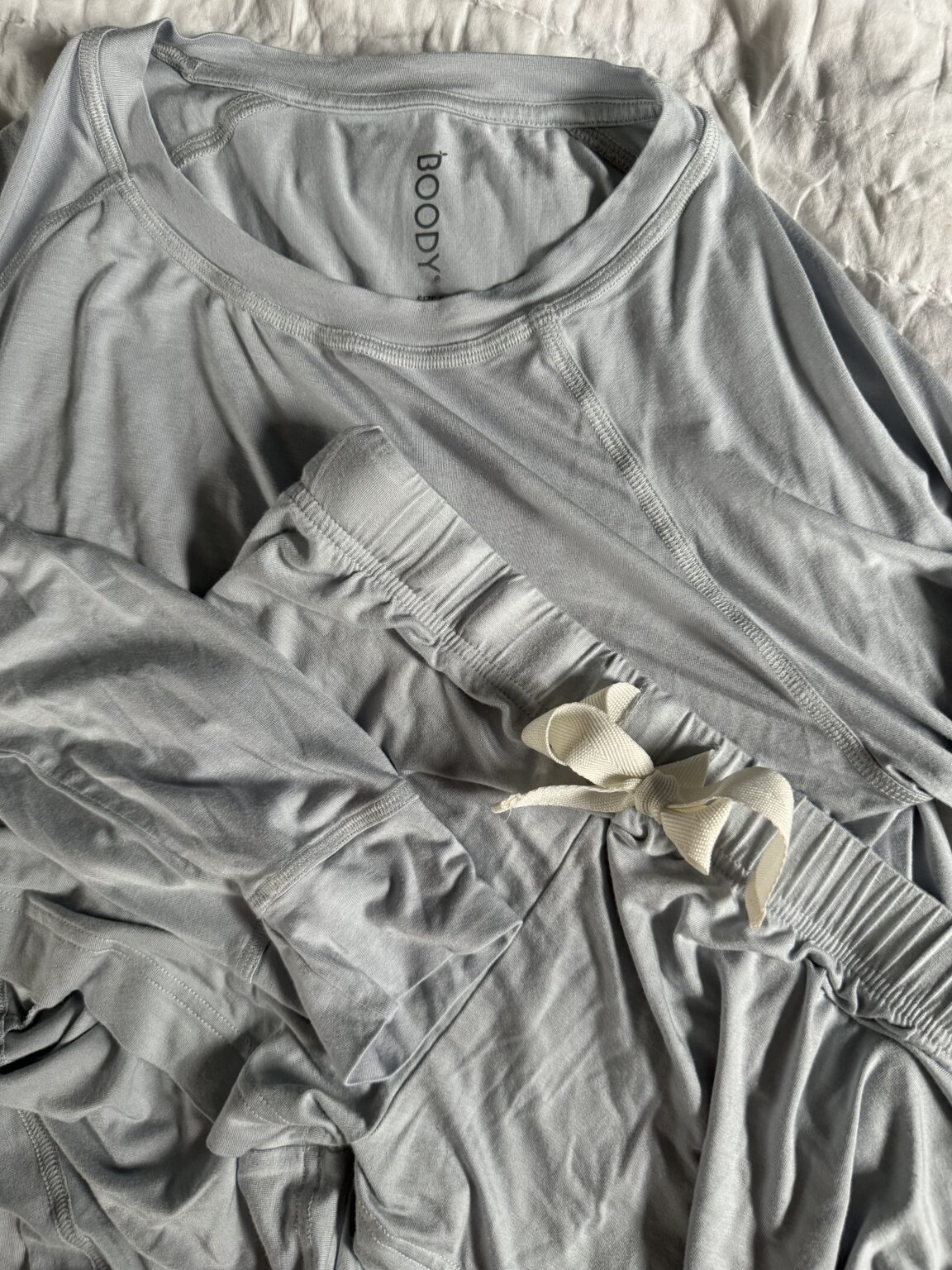 Light gray long-sleeve shirt and elastic-waist pants with a drawstring, both made of soft fabric, laid out on a white surface.