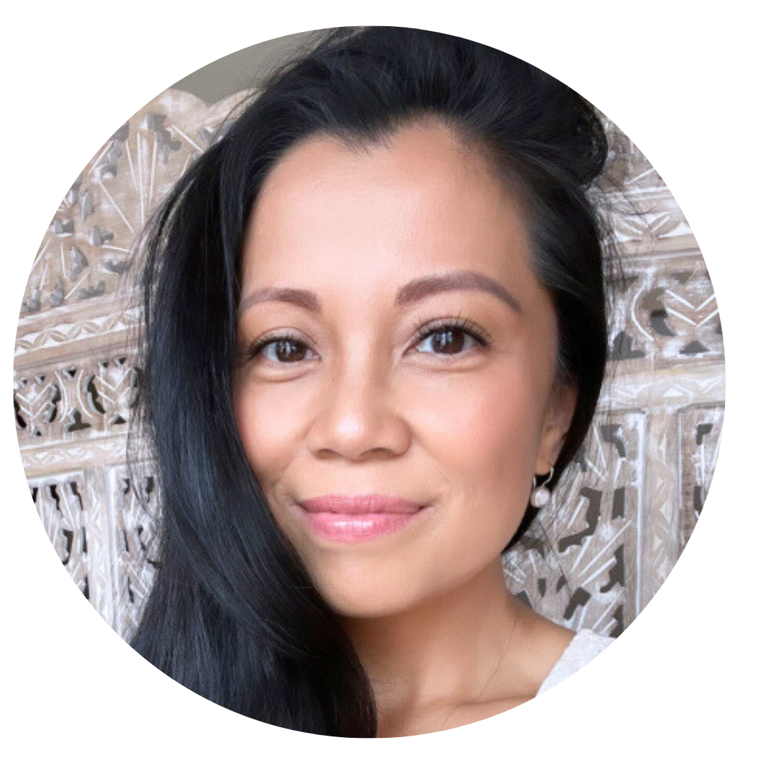 Woman with long black hair, light makeup, and pearl earrings smiling softly in front of a decorative, carved background.