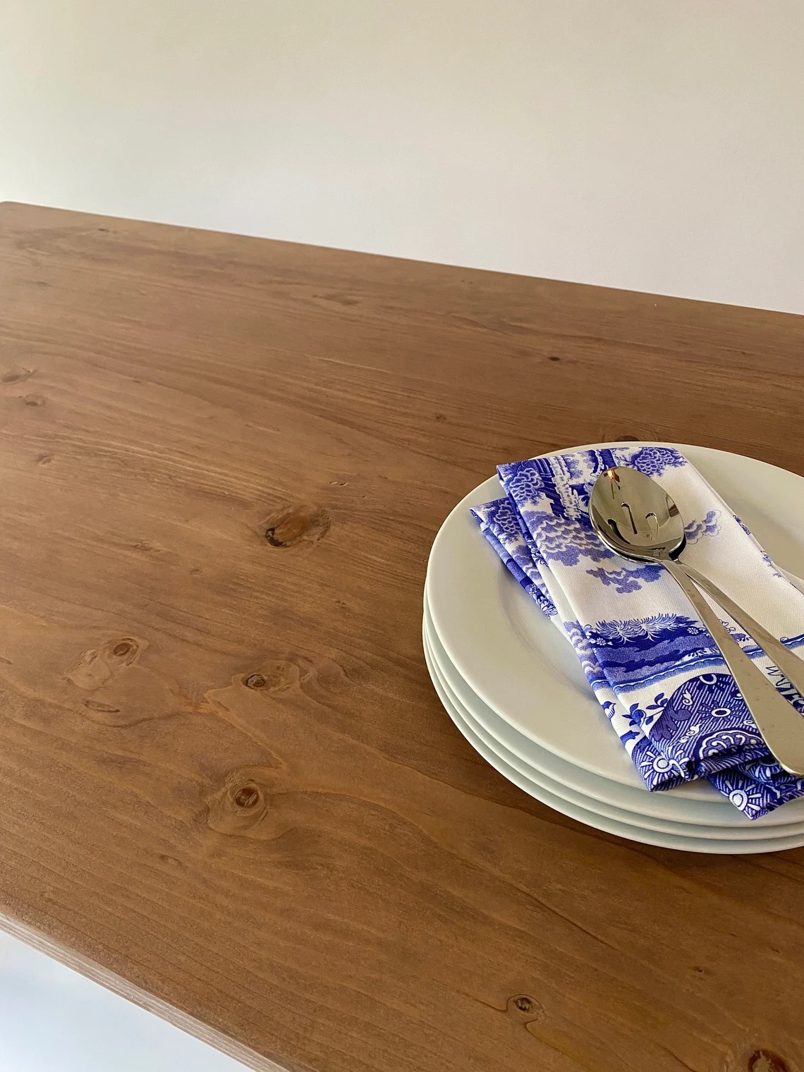 Three white plates stacked with a blue and white napkin, fork, and spoon on a wooden table.