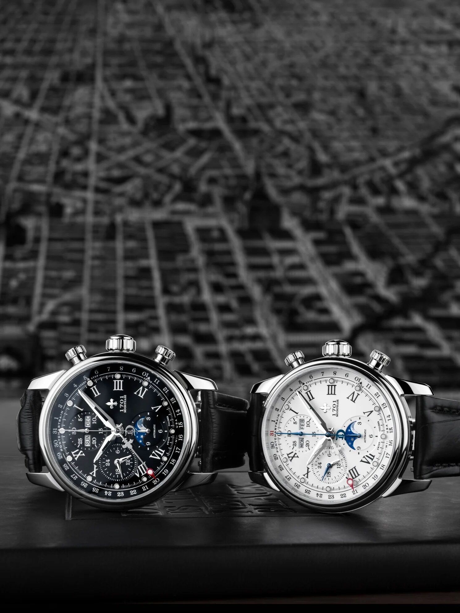 Two luxury chronograph wristwatches with leather straps, one with a black dial and the other with a white dial, displayed side by side on a black surface.